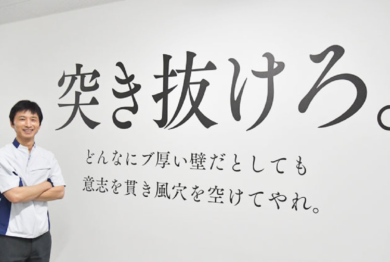 「突き抜けろ。」と大きく書いてある壁に立つ榊原さん